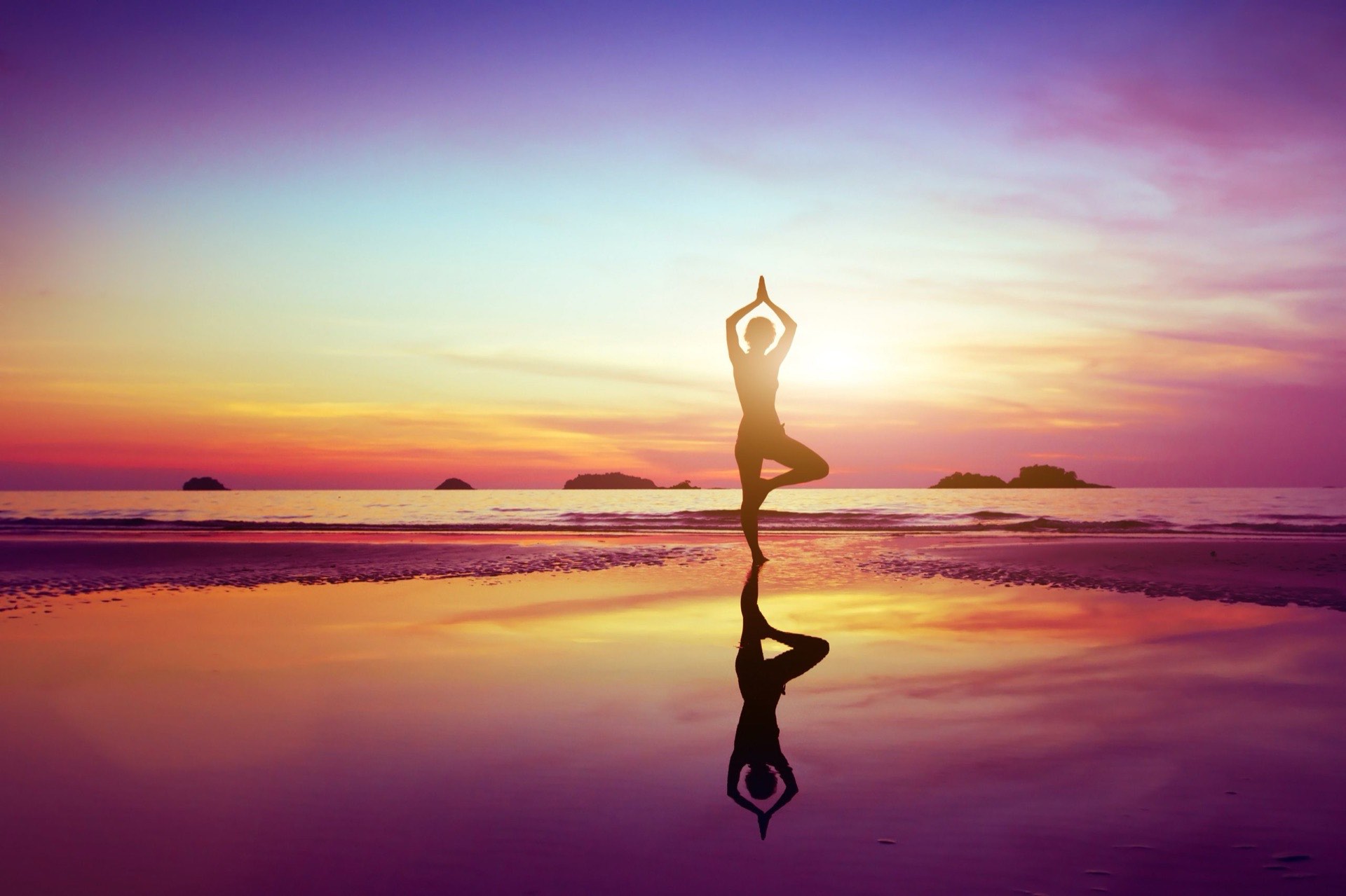 A person in a yoga tree pose reflected on a beach at sunrise