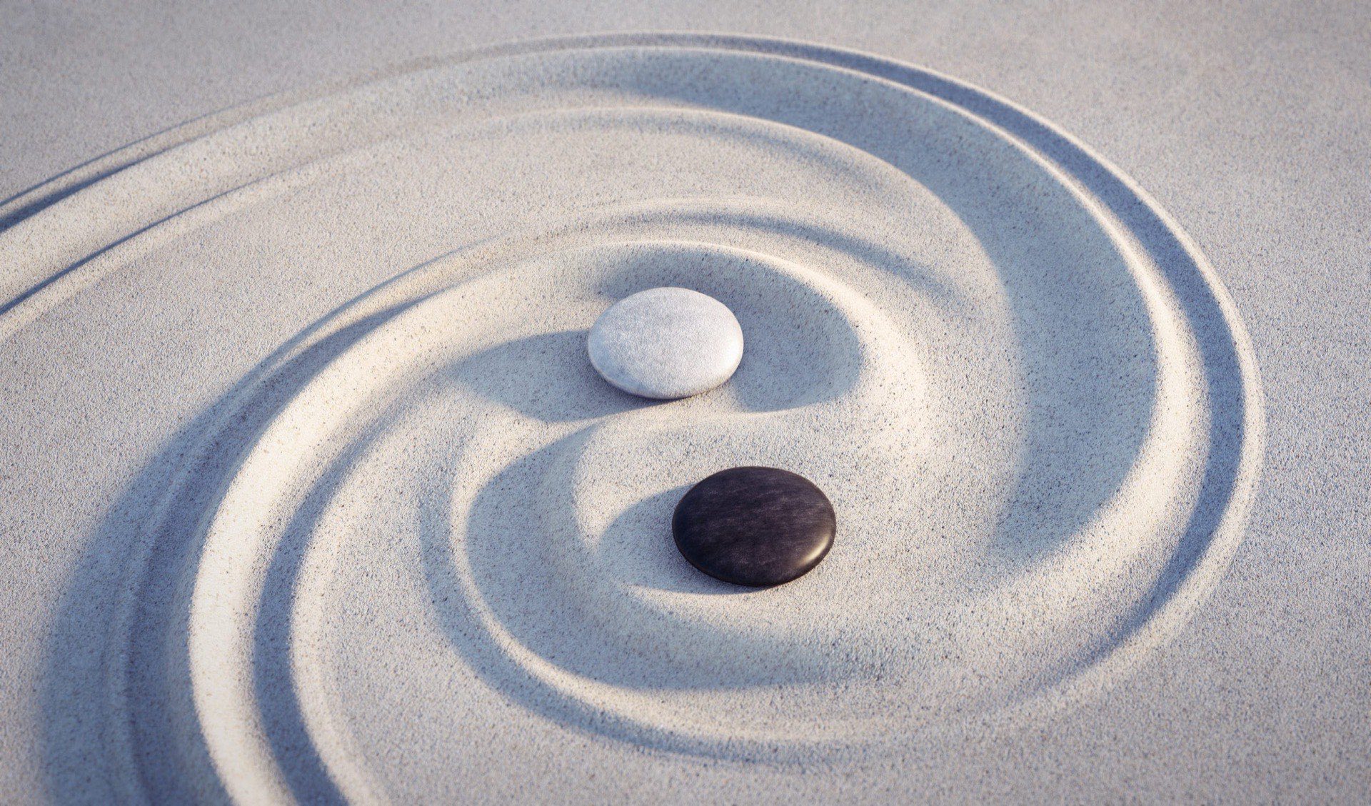 Two smooth stones on raked sand forming a yin and yang pattern