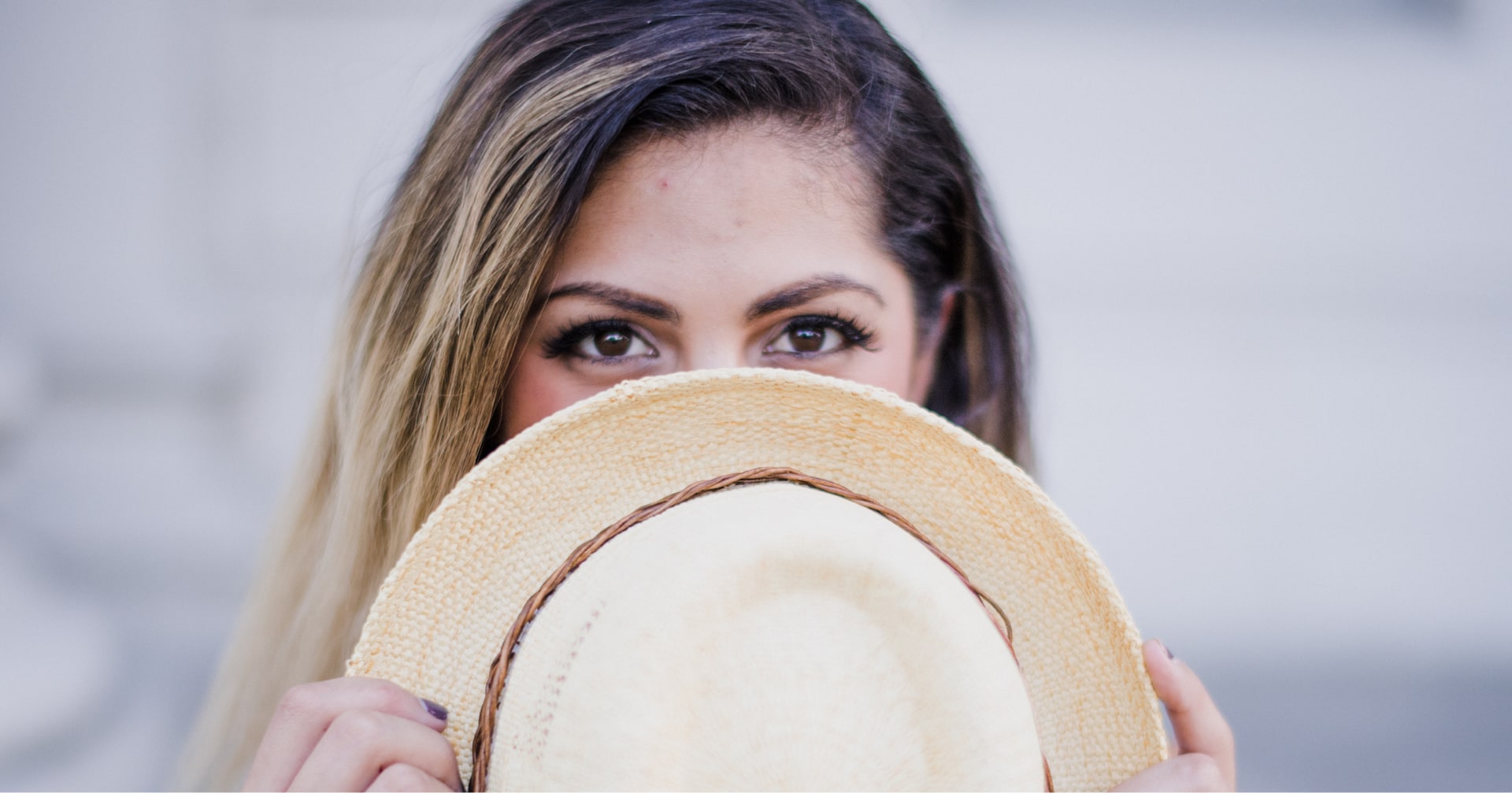 A woman holding a straw hat in front of her face outdoors