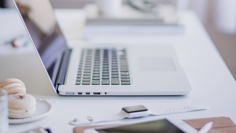 A laptop, smartwatch and tablet on a bright white desk